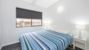 A bedroom with a bed, a nightstand, a lamp, a window with a blind, and a ceiling light. - Cape Marengo (Marengo)