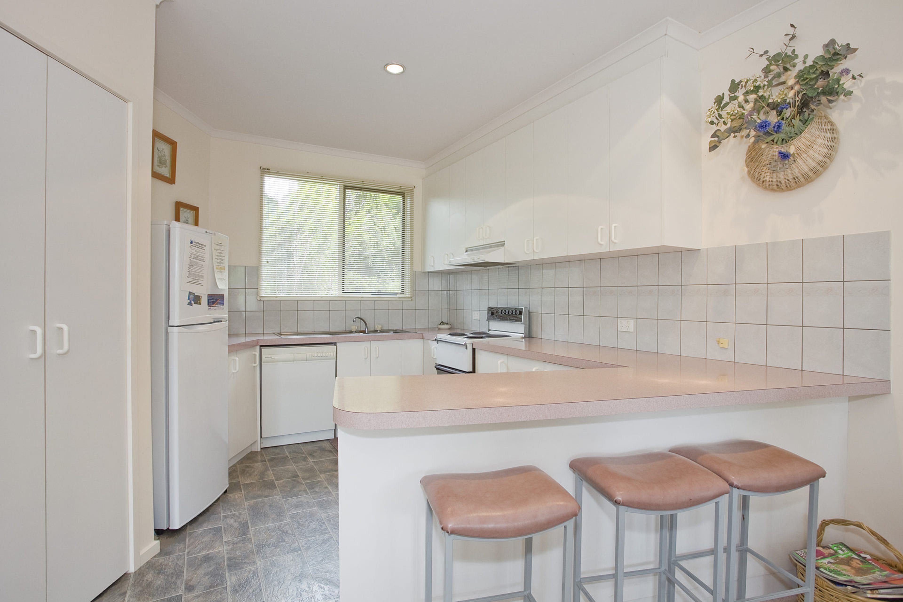 A kitchen with white cabinets, a refrigerator, a stove, and a window with blinds.