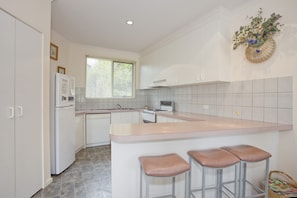 A kitchen with white cabinets, a refrigerator, a stove, and a window with blinds.