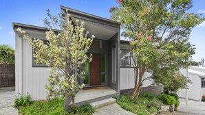 Une maison moderne à deux étages, dotée d’un porche à l’avant, d’une porte verte et d’un petit jardin agrémenté de plantes à fleurs.