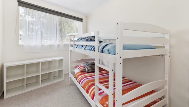 Une chambre avec un lit superposé, une fenêtre, un banc blanc et une étagère.