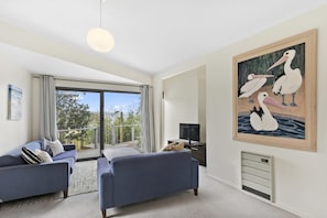 A modern living room with a large window, a sofa set, a flat-screen TV, and a painting of pelicans.
