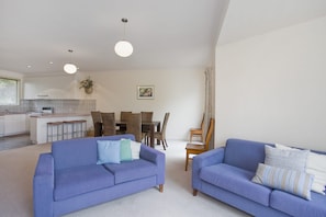 A modern living room with two sofas, a dining area with a table and chairs, and a kitchen in the background.