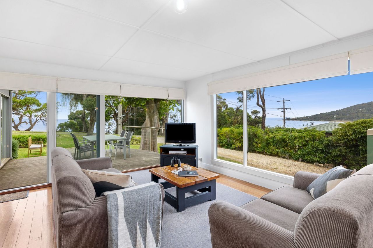 A modern living room with a large sliding glass door leading to an outdoor deck, a flat-screen TV, and a wooden coffee table.