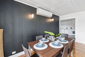 Un coin repas avec un mur de couleur sombre, un plafond blanc et une cuisine en arrière-plan.