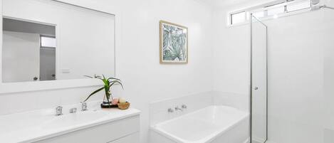 A modern bathroom with a white vanity, a bathtub, and a glass-enclosed shower.