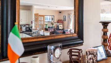 A room with a large mirror reflecting a kitchen area, a flag, a clock, and a framed photo on a wooden table.
