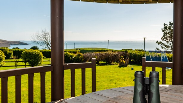 Een houten terras met verrekijkers op een tafel, met uitzicht op een grasveld en de zee.