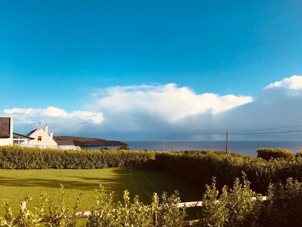 Una casa de fachada blanca, césped cuidado y vista al mar.