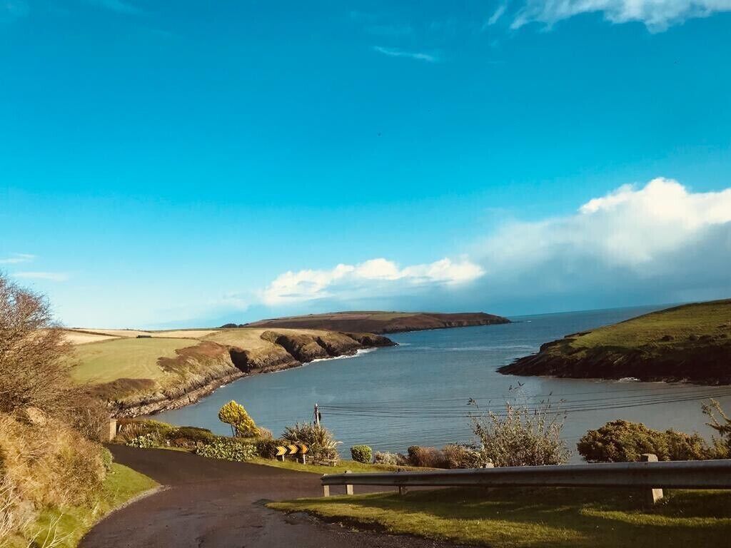 Una carretera costera con barandilla, cielo despejado y vista al mar.