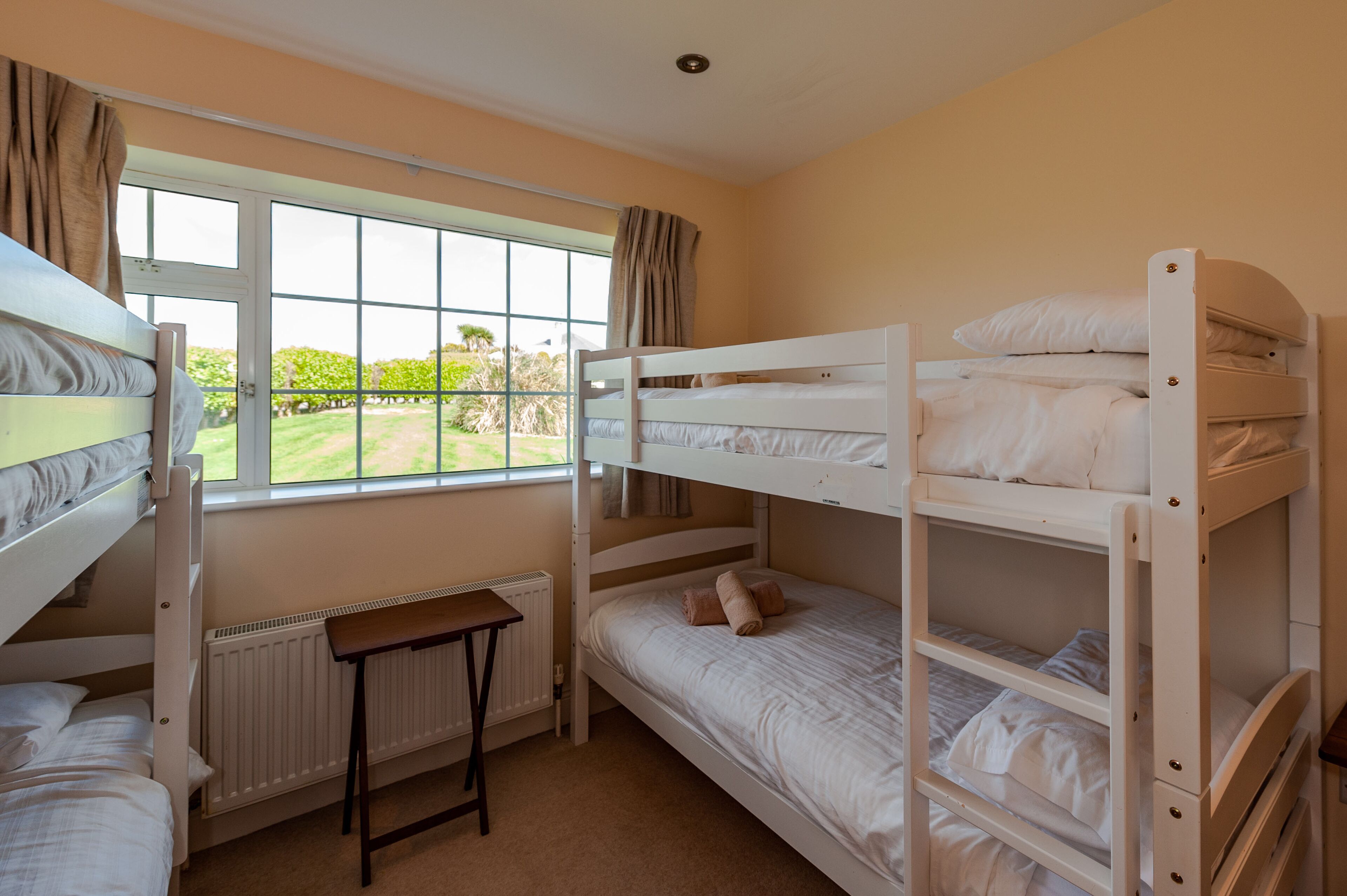A bunk bed room with a window, a radiator, and a small table.