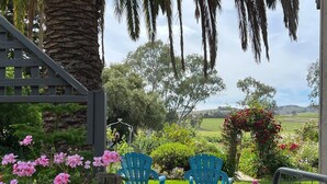 A wooden deck with two blue chairs, surrounded by lush greenery and flowering plants. - Azalea Cedar-Rose Villa (Lyndoch)