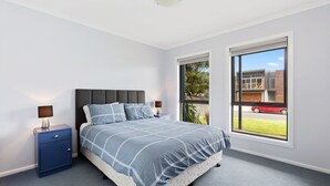 A bedroom with a bed, a nightstand, a window, and a view of the outside.