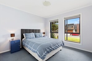 A bedroom with a bed, a nightstand, a window, and a view of the outside.