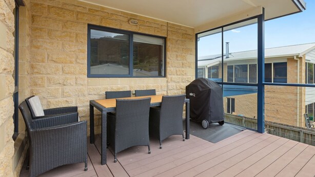 A covered outdoor seating area with a table and chairs, a grill, and a view of the surrounding buildings.