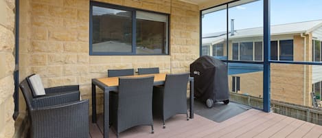 A covered outdoor seating area with a table and chairs, a grill, and a view of the surrounding buildings.