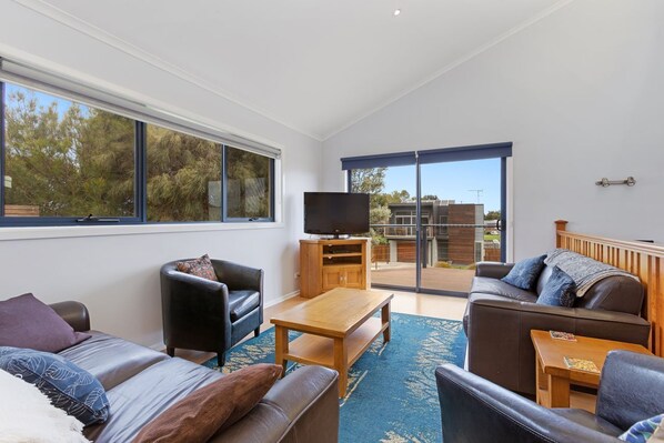 A modern living room with a sofa, armchair, and coffee table, a television, and a large sliding glass door leading to an outdoor area.