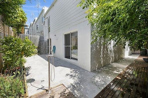 A residential outdoor area with a concrete patio, a wooden deck, and a white house with a sliding glass door.