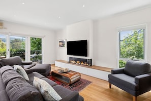 A modern living room with a flat-screen TV, a fireplace, a sofa, and a chair.