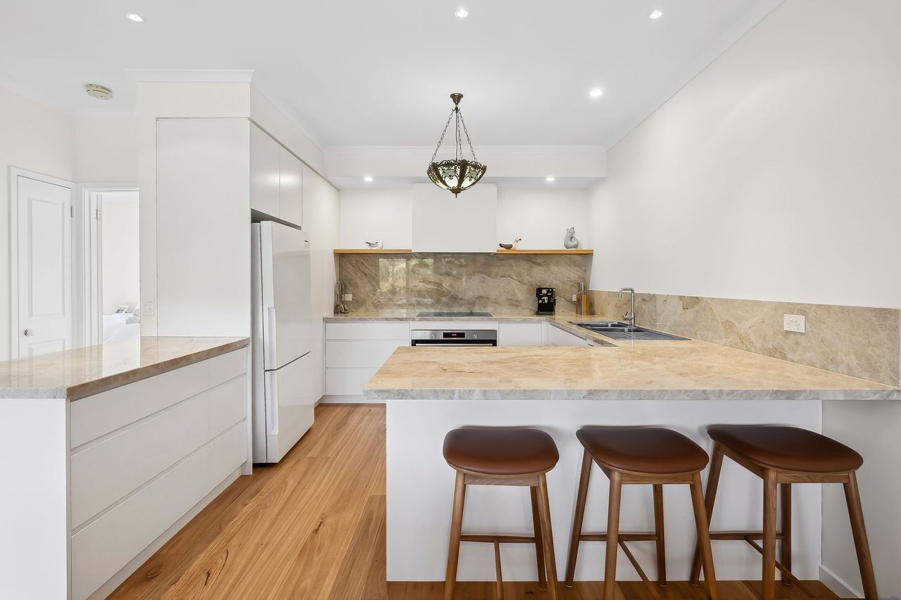 A modern kitchen with white cabinetry, a marble countertop, and a built-in oven.