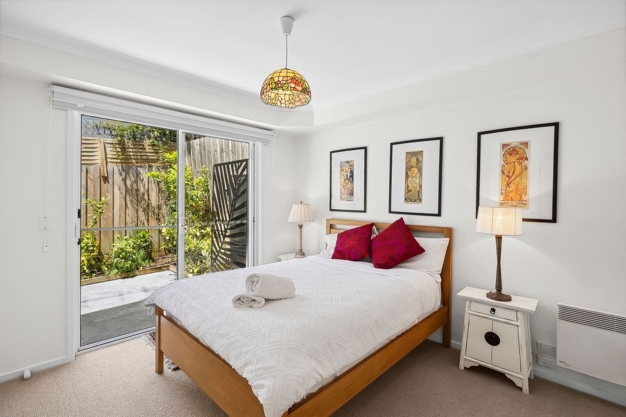 A bedroom with a bed, a nightstand, a lamp, and a sliding glass door leading to a balcony.
