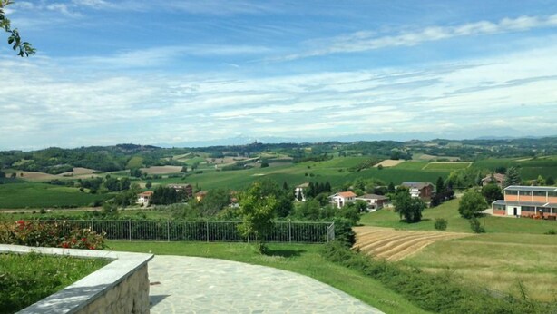 A stone-paved terrace with a stone wall on one side, overlooking a rural landscape with fields and houses. - Fantastic house in Monferrato! (Tonco)