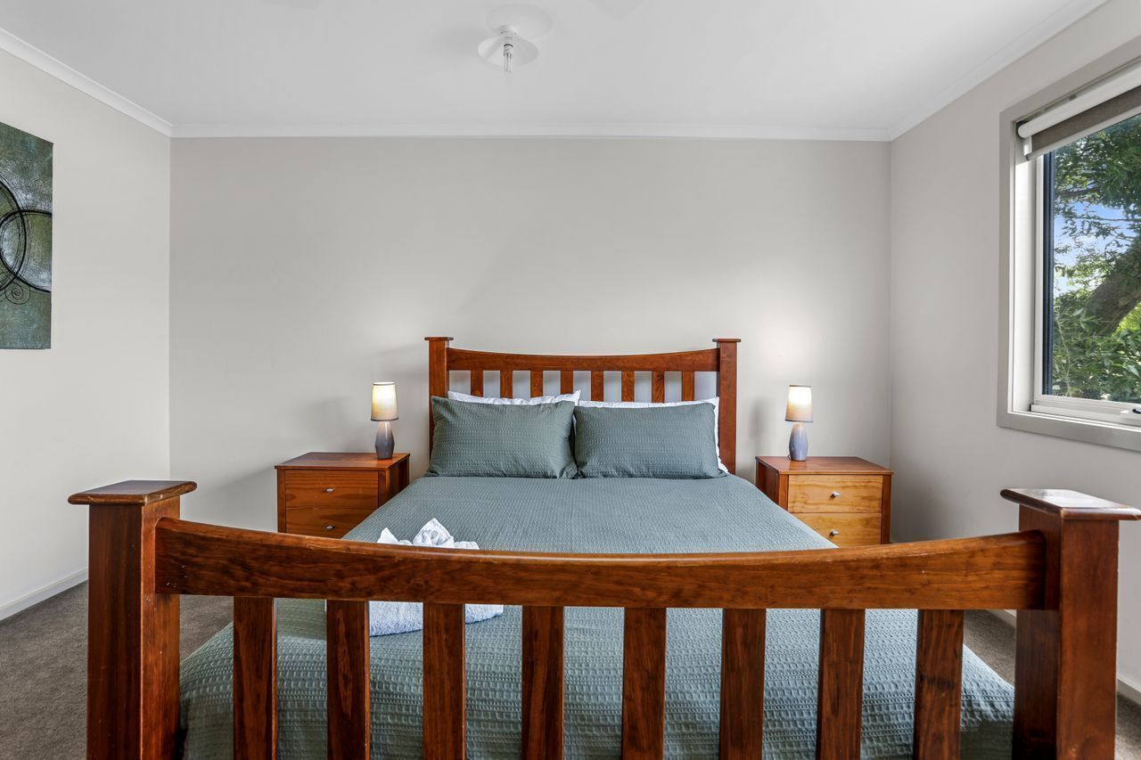 A bedroom with a wooden bed, two bedside tables, a window, and a wall-mounted artwork.
