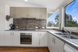 A modern kitchen with white cabinets, a stainless steel sink, and a large window. - Number 6 at The Bay (Apollo Bay)