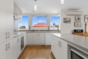 A modern kitchen with white cabinetry, a large window, and a view of a red-roofed building. - Number 6 at The Bay (Apollo Bay)