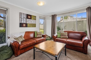 A living room with two leather sofas, a wooden coffee table, and a wall art piece. - Number 6 at The Bay (Apollo Bay)