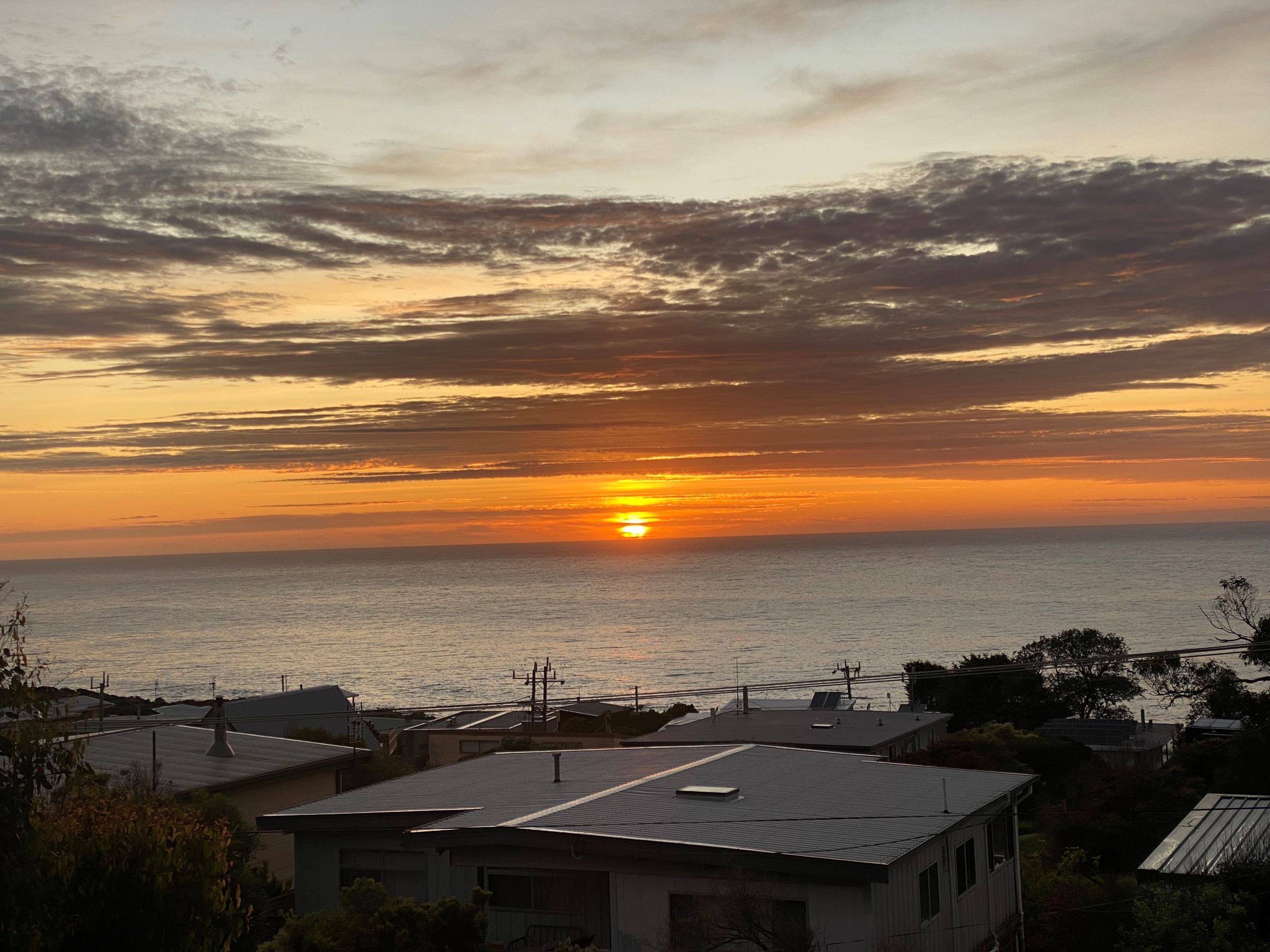 Ein Sonnenuntergang über dem Meer mit Wohngebäuden im Vordergrund.