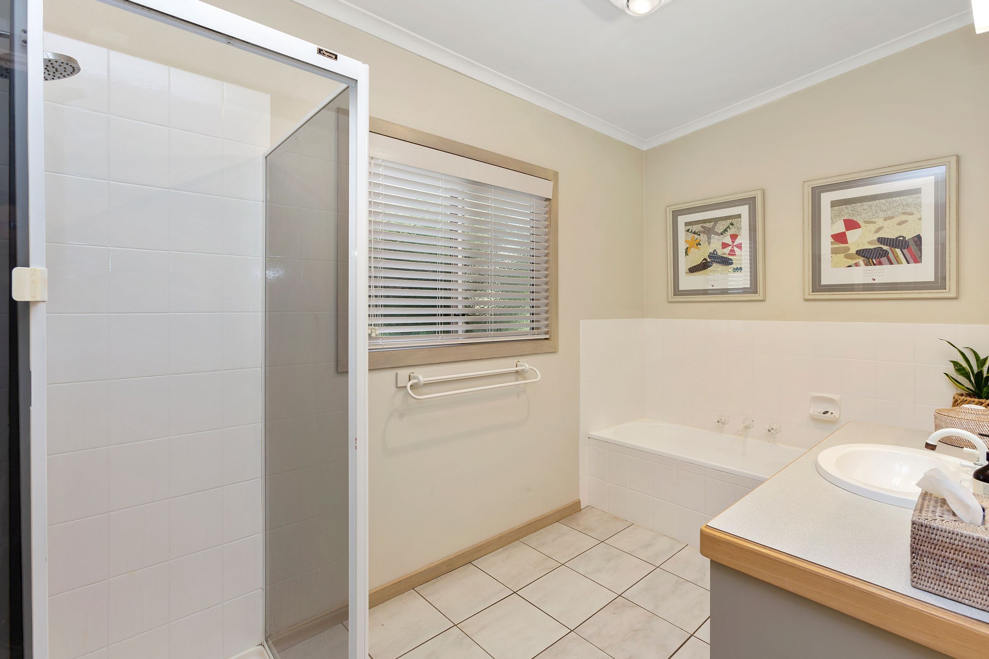 Une salle de bain équipée d’une douche, d’une baignoire, d’un lavabo et de deux tableaux encadrés accrochés au mur.