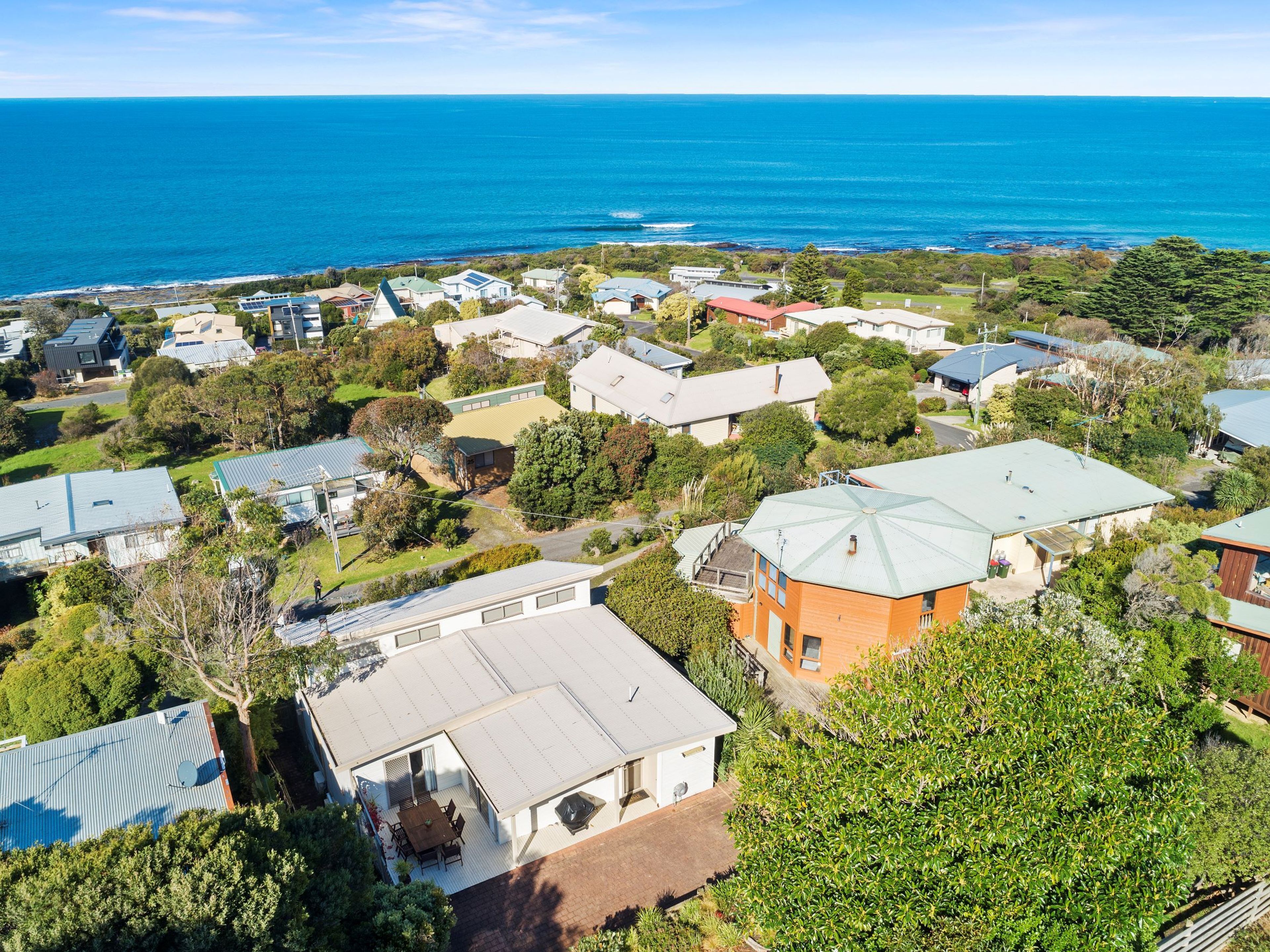Vue aérienne d’un quartier résidentiel situé sur la côte, avec des maisons, dont certaines sont dotées de toits végétalisés, et une vue dégagée sur l’océan.