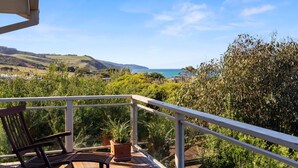 Ein Balkon mit einem Holzstuhl und einer Topfpflanze, mit Blick auf eine Küstenlandschaft mit Hügeln und dem Meer.