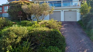 Ein Wohnhaus mit gepflasterter Auffahrt, die zu einer Garage führt, umgeben von üppiger Bepflanzung und alten Bäumen.