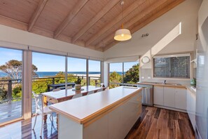 A modern kitchen with a large island, wooden flooring, and a view of the ocean. - Otway Views (Skenes Creek)