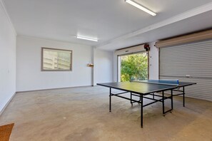 A room with a ping pong table, a window with blinds, and a view of greenery outside. - Otway Views (Skenes Creek)