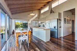 A modern kitchen with a large island, wooden flooring, and a view of greenery outside.