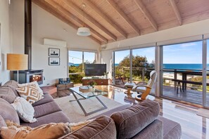 A spacious living room with a large sofa, a flat-screen TV, and a view of the sea through large windows. - Otway Views (Skenes Creek)