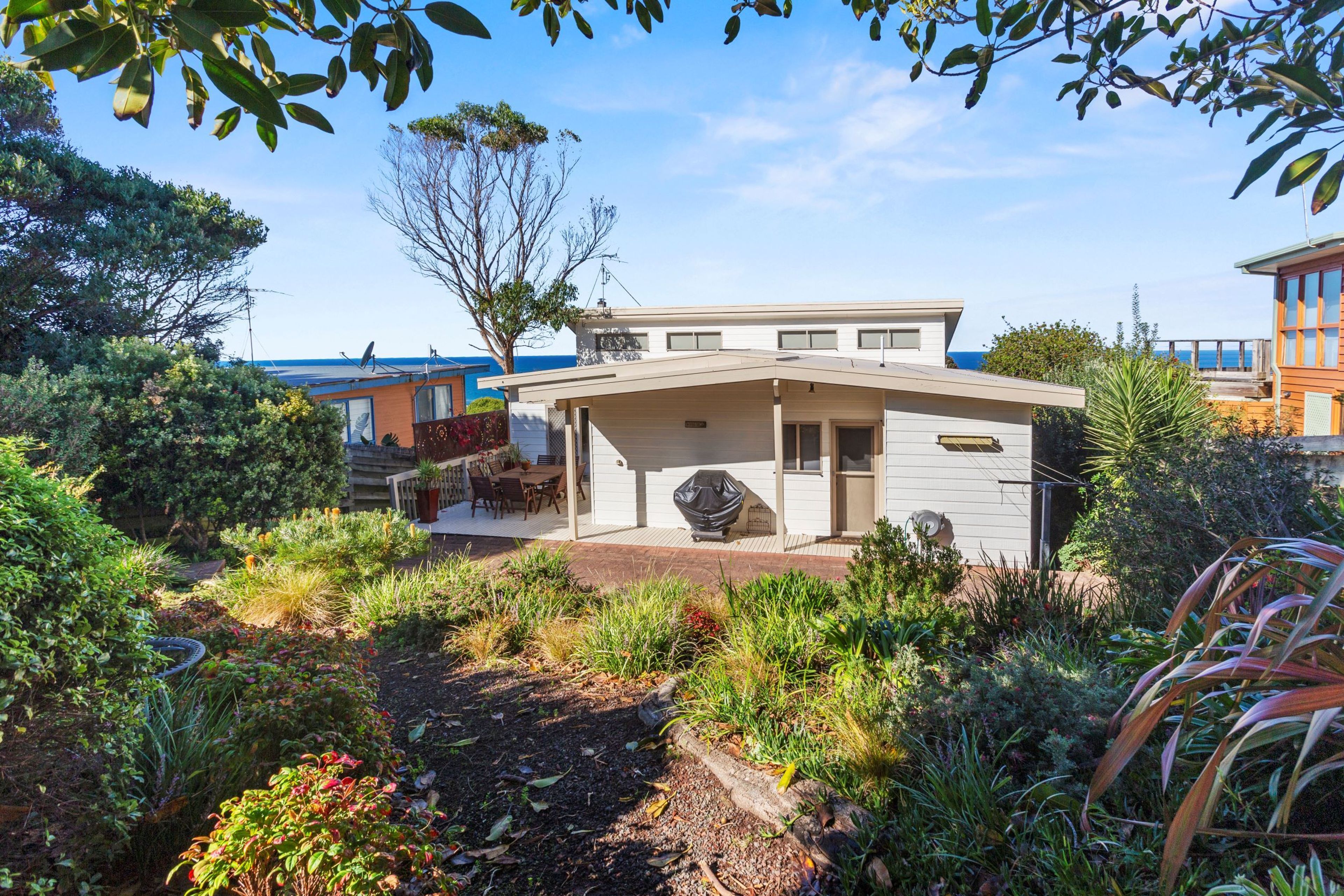 A modern house with a covered patio, surrounded by lush garden vegetation.