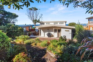 A modern house with a covered patio, surrounded by lush garden vegetation.