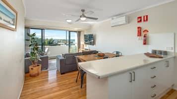 A modern kitchen with a large island, dining area with a table and chairs, a sofa, and a balcony with a view.