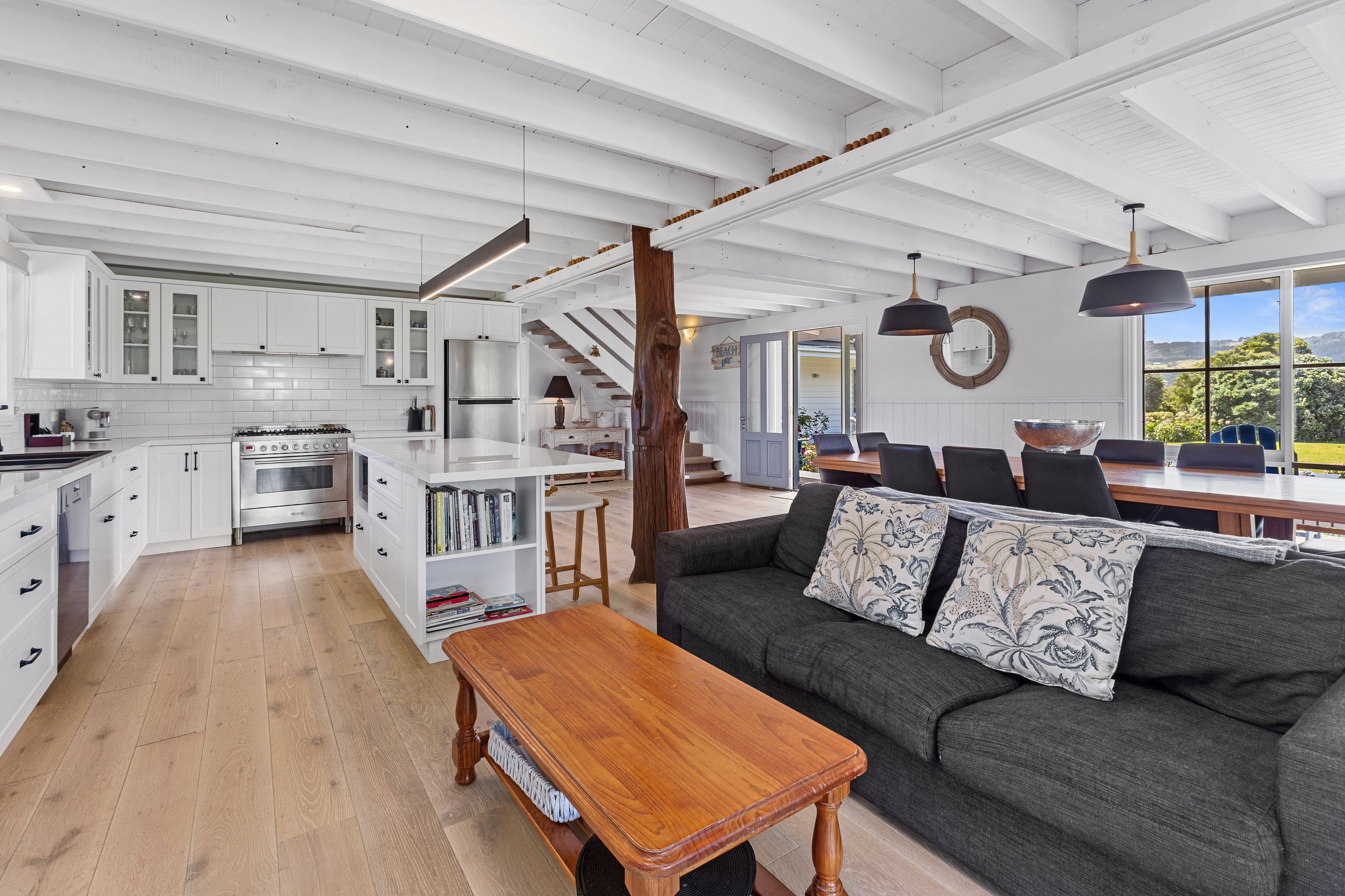 A spacious living area with a wooden coffee table, a gray sofa with patterned cushions, and a view of the outdoors through large windows.