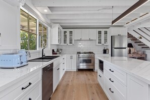 A modern kitchen with white cabinetry, stainless steel appliances, and a wooden floor.