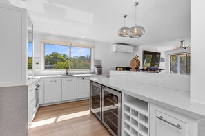 A modern kitchen with white cabinetry, a built-in dishwasher, and a large window offering a view of greenery. - The Great Escape (Marengo)