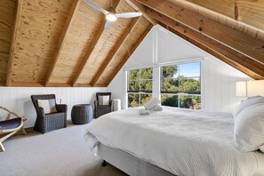 A bedroom with a sloped ceiling, a large bed, a chair, a small table, and a window with a view of greenery. - The Great Escape (Marengo)