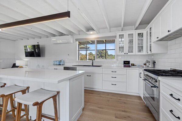 A modern kitchen with white cabinetry, a large island with bar stools, a built-in oven, and a window providing a view of the outdoors.