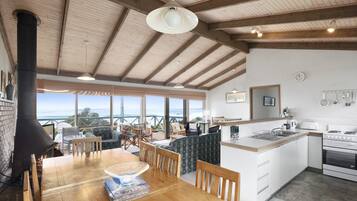 A spacious kitchen with a large island, wooden beams on the ceiling, and a view of the ocean through large windows.