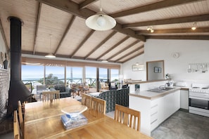 A spacious kitchen with a large island, wooden beams on the ceiling, and a view of the ocean through large windows.