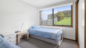 A bedroom with a single bed, a bedside table with a lamp, a dresser, and a window with a view of a green landscape. - Seamoon - Apollo Bay (Apollo Bay)